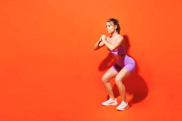 Fototapeta na wymiar Full body side view young fitness trainer woman sportsman wears top shorts purple clothes in home gym do squats look aside on area isolated on plain orange background. Workout sport fit abs concept.