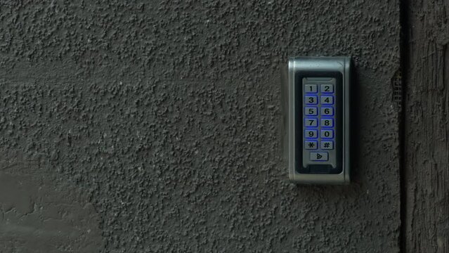 A closeup of an electric blue keypad on a grey concrete wall