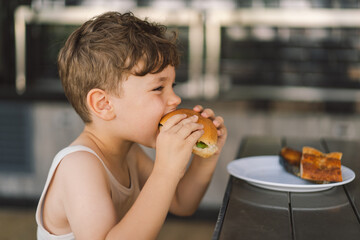 Little Boy Eating Sandwich and French Fries at Table - obrazy, fototapety, plakaty