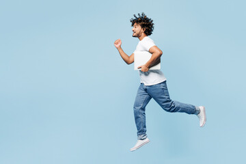 Full body young happy IT Indian man wear white t-shirt casual clothes jump high hold laptop pc computer run fast hurry up isolated on plain pastel light blue cyan background studio. Lifestyle concept.