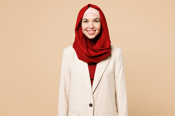 Young smiling happy Arabian Asian Muslim woman wearing red abaya hijab suit clothes looking camera isolated on plain beige wall background studio portrait. UAE middle eastern Islam religious concept.