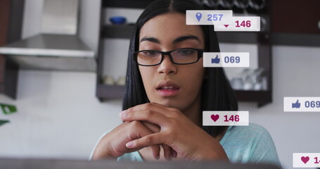 Image of social media icons and numbers over biracial woman using laptop