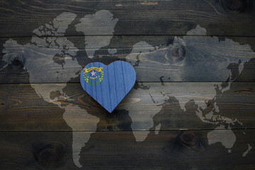 wooden heart with national flag of nevada state near world map on the wooden background.