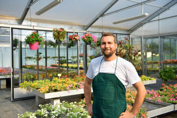 happy worker growing flowers in a greenhouse of a flower shop - 785396460