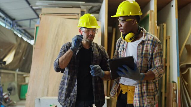 Front view of African American carpenter or woodworker or charpentier man use tablet to consult and discuss with coworker as coach or support staff during work in workplace.