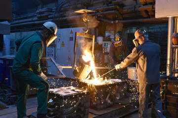 Group of workers in an iron foundry - casting a workpiece with liquid hot metal into a mold - cooperation and work safety - 785398271