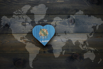 wooden heart with national flag of oklahoma state near world map on the wooden background.