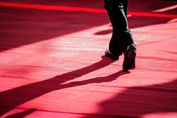 Person walking on red carpet with shadow of legs on ground underneath sunset sky