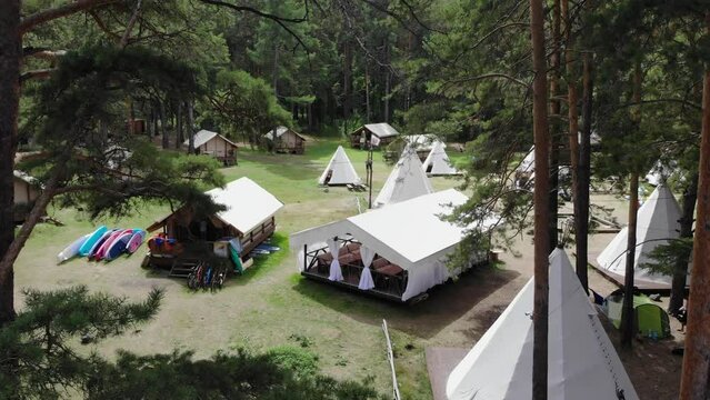 An open-air cafe amidst yurts and teepees in a tourist camp surrounded by pine forest. Aerial footage. 4k
