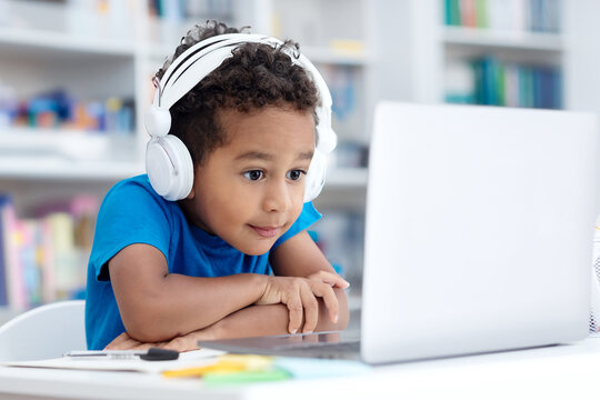 Enthusiastic primary school boy wearing headphones, looking at computer screen, learning using laptop software application