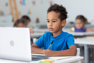 Focused primary school pupil african american schoolboy using laptop in classroom interior, studying at lesson