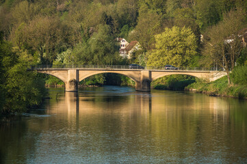 Rundbogenbrücke im Morgenlicht mit Reflexionen im Fluss

