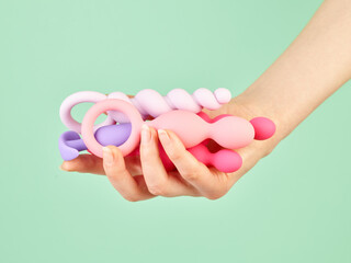 Woman's hand holding adult sex toys over mint background