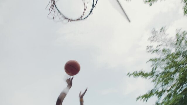 Handheld slowmo of male African American sportsman bouncing and throwing ball in ring while playing streetball outdoors