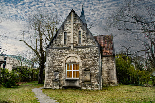 Eine alte Friedhofskappelle aus Stein. Mit den noch kahlen B&auml;umen und dem wolkigem Himmel wirkt es fast  etwas grusselig  