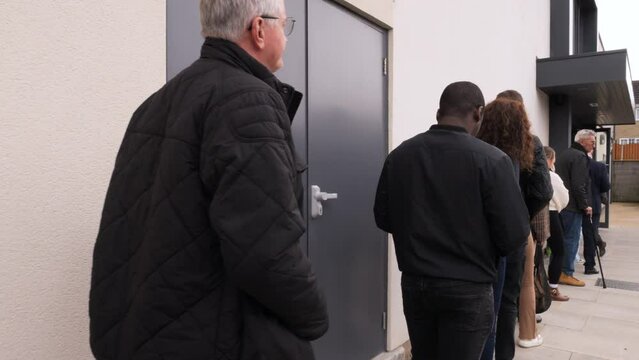 4K: People stand in line outside stood waiting.  People queuing up looking impatient. Back view. Stock Video Clip Footage