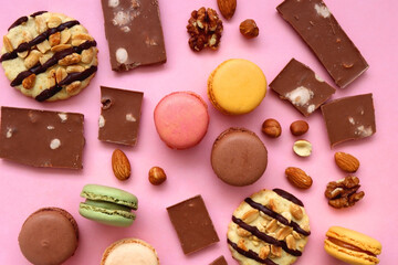 Pastel macarons, almond chocolate, peanut butter cookies and various nuts on bright pink background. Top view.
