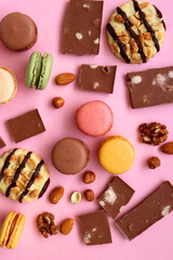 Pastel macarons, almond chocolate, peanut butter cookies and various nuts on bright pink background. Top view.