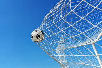 Naklejka premium Soccer ball in soccer goal net in a big stadium isolated on blue sky. soccer net.