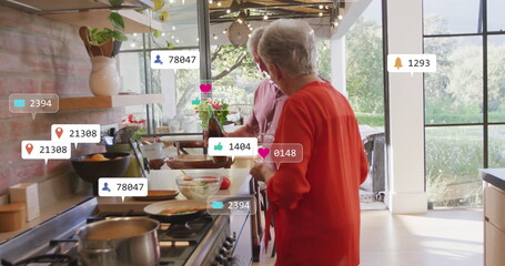 Image of social media text and icons over senior caucasian couple in kitchen at home