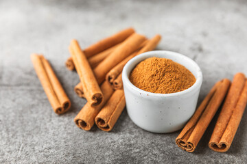Cinnamon powder in a bowl on a textured wooden background. Spicy spice for baking, desserts and drinks. Fragrant ground cinnamon. Cinnamon stick. Place for text. Copy space.