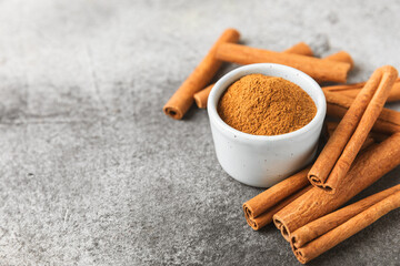 Cinnamon powder in a bowl on a textured wooden background. Spicy spice for baking, desserts and drinks. Fragrant ground cinnamon. Cinnamon stick. Place for text. Copy space.