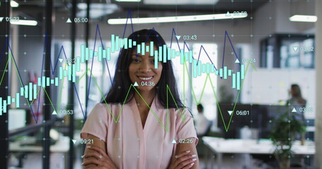Image of multiple graphs with changing numbers over smiling biracial woman standing arms crossed