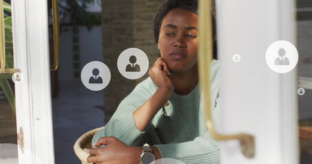 Image of profile icon in circles over thoughtful african american woman looking through window - Powered by Adobe