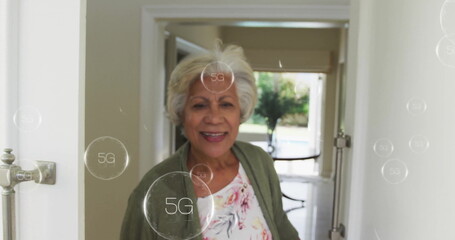 Image of 5g text in circles over senior smiling biracial woman opening door of house - Powered by Adobe