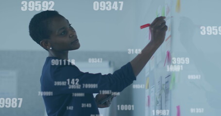 Image of numbers processing over businesswoman writing on whiteboard in office