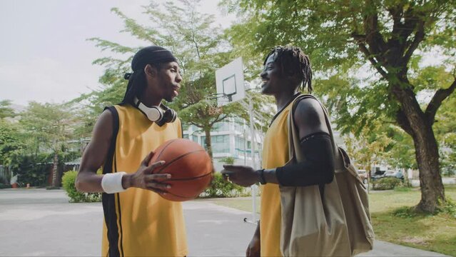 Medium long shot of two sportsmen of African American ethnicity chatting after game on streetball outdoor playground