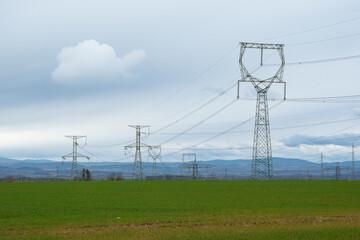 high voltage pylons on a meadow under cloudy skies