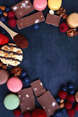Macarons, chocolate, cookies, berries and various nuts on dark blue background. Top view.