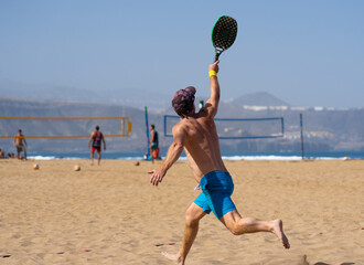 Mature male beach tennis player playing a match. Summer sports