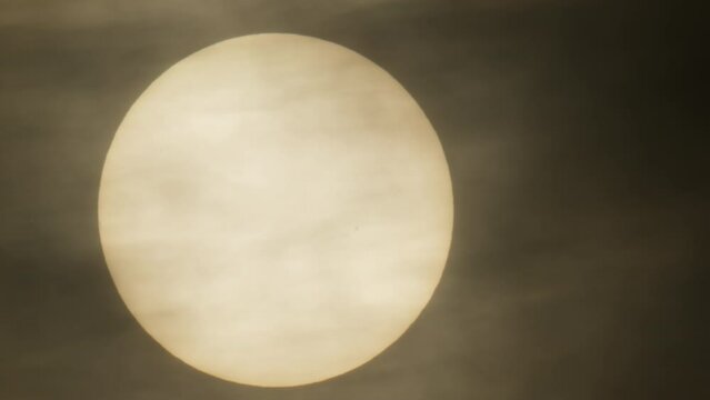 Close-up of the sun hidden by a thin layer of dark clouds