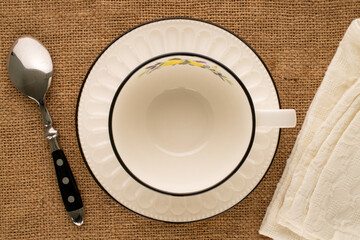 One white porcelain cup with saucer, spoon and napkin on jute cloth, macro, top view. - Powered by Adobe