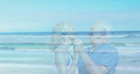 Fototapeta premium Image of landscape with ocean over happy senior caucasian couple dancing at beach