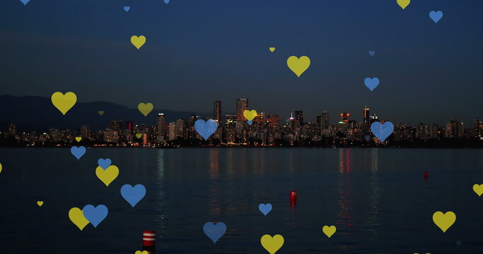 Image of yellow and blue hearts floating over night cityscape
