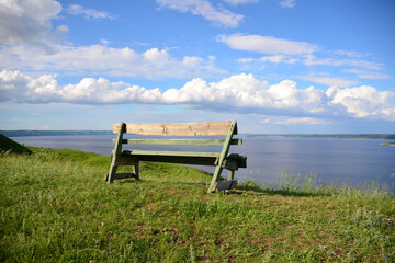 a wooden bench on the edge of the hill with cloudscape on background  