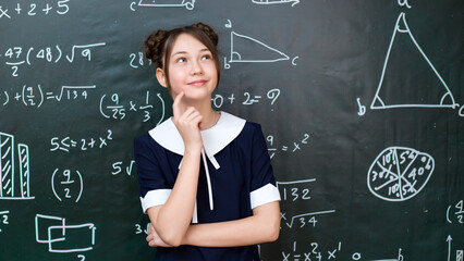 A teenage schoolgirl is thinking while standing blackboard, a 10-12 year old girl is solving a math problem.
