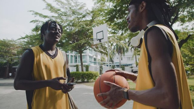 Medium shot of black men spending time together on basketball playground outdoors