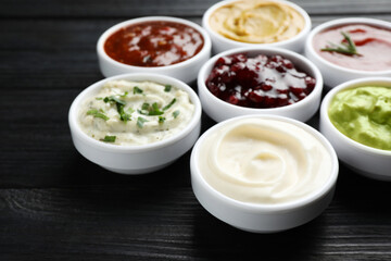 Different tasty sauces in bowls on black wooden table, closeup