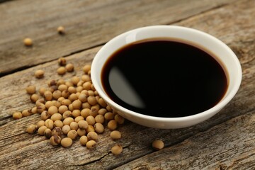 Soy sauce in bowl and beans on wooden table, closeup