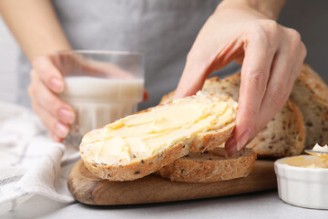 Woman taking slice of bread with tasty butter at table, closeup