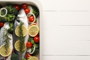 Raw fish with vegetables and lemon in baking dish on white wooden table, top view. Space for text