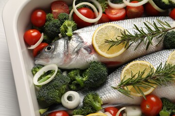 Raw fish with vegetables and lemon in baking dish on white table