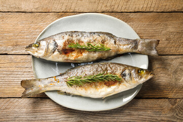 Delicious baked fish and rosemary on wooden table, top view