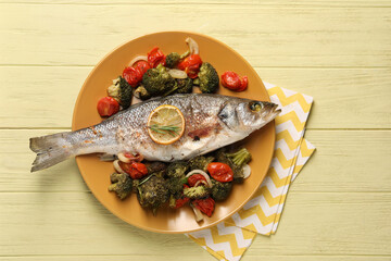 Delicious baked fish and vegetables on yellow wooden table, top view