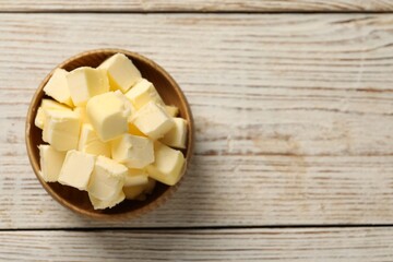 Tasty butter cubes in bowl on light wooden table, top view. Space for text