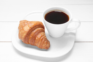 Tasty breakfast. Cup of coffee and croissant on white wooden table